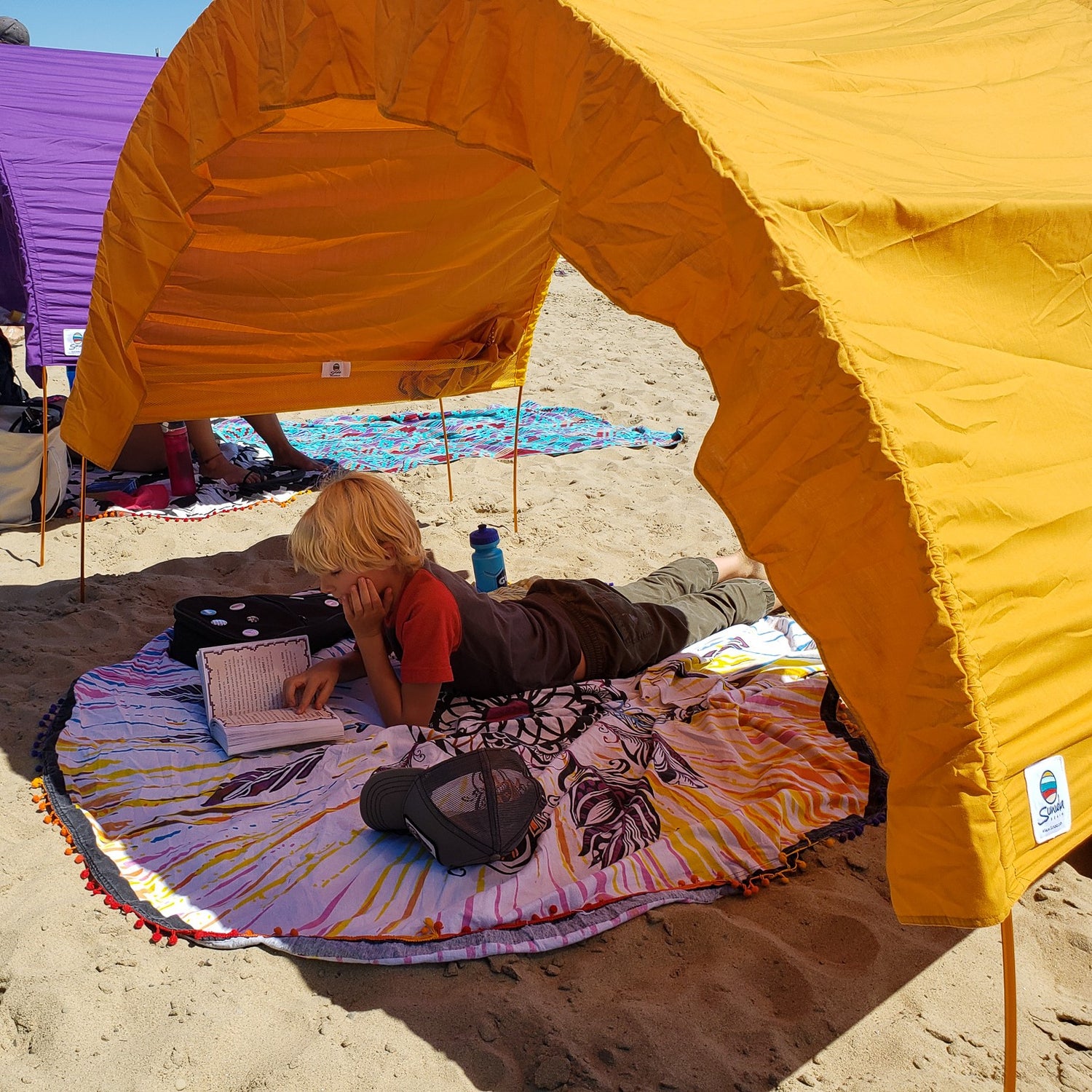 little boy reads a book while laying on a cotton beach roundie by Suniela