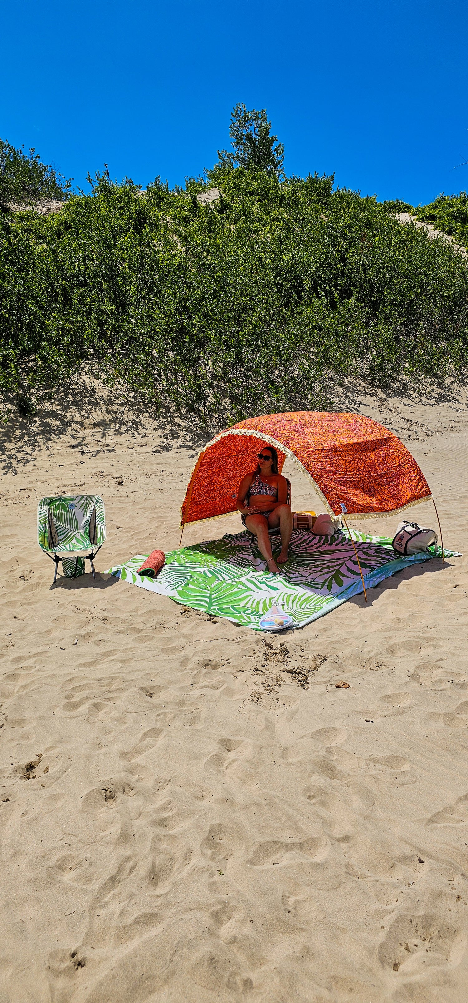 woman sits on a beach chair in the shade beneath her Suniela sun shelter