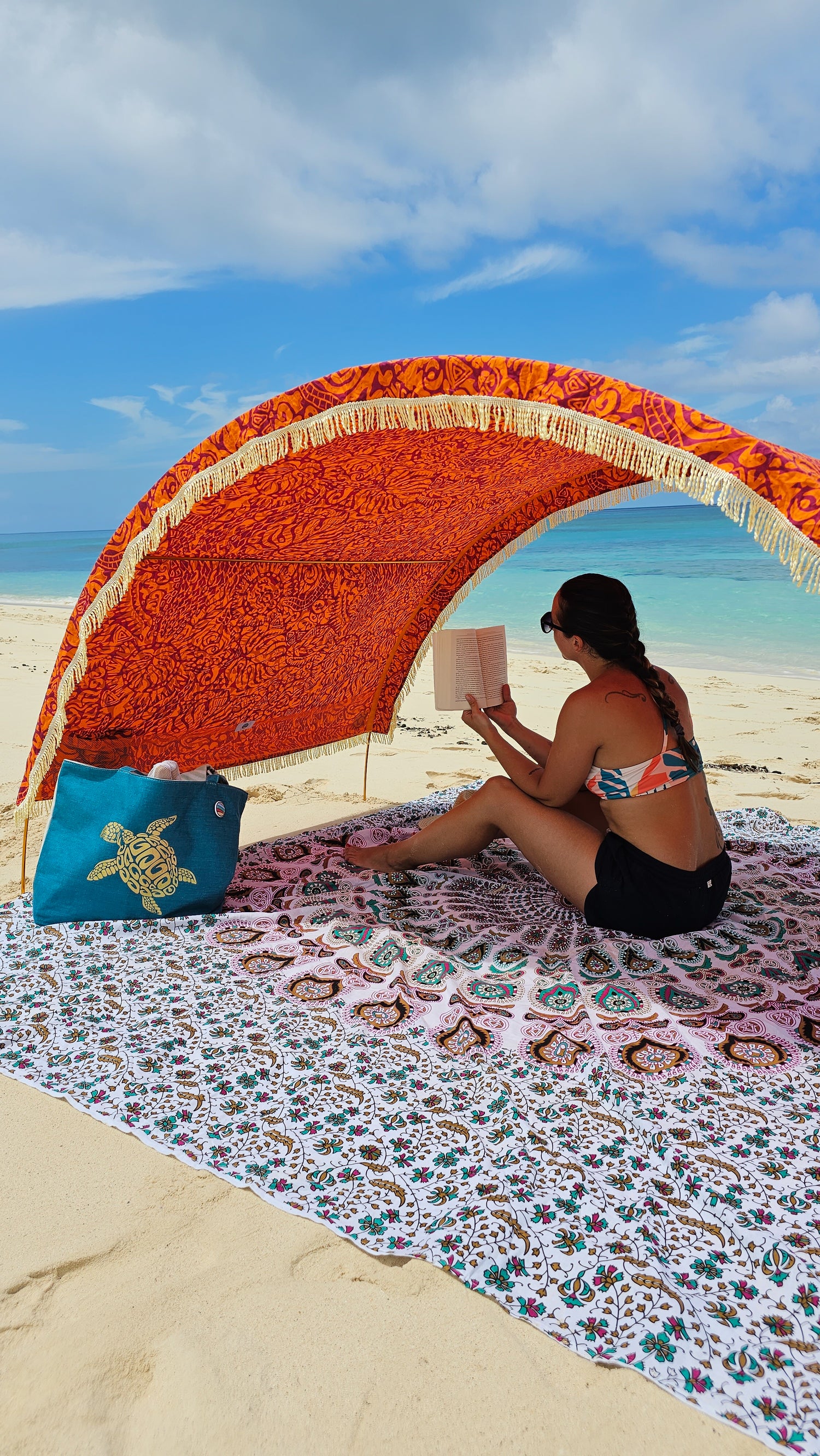 woman reads a book in the shade while sitting on a cotton beach mat by Suniela