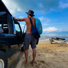 Man gets out of his jeep on the sand carrying a Suniela cabana in it's compact carry bag over his shoulder_printTurquoiseSuniela